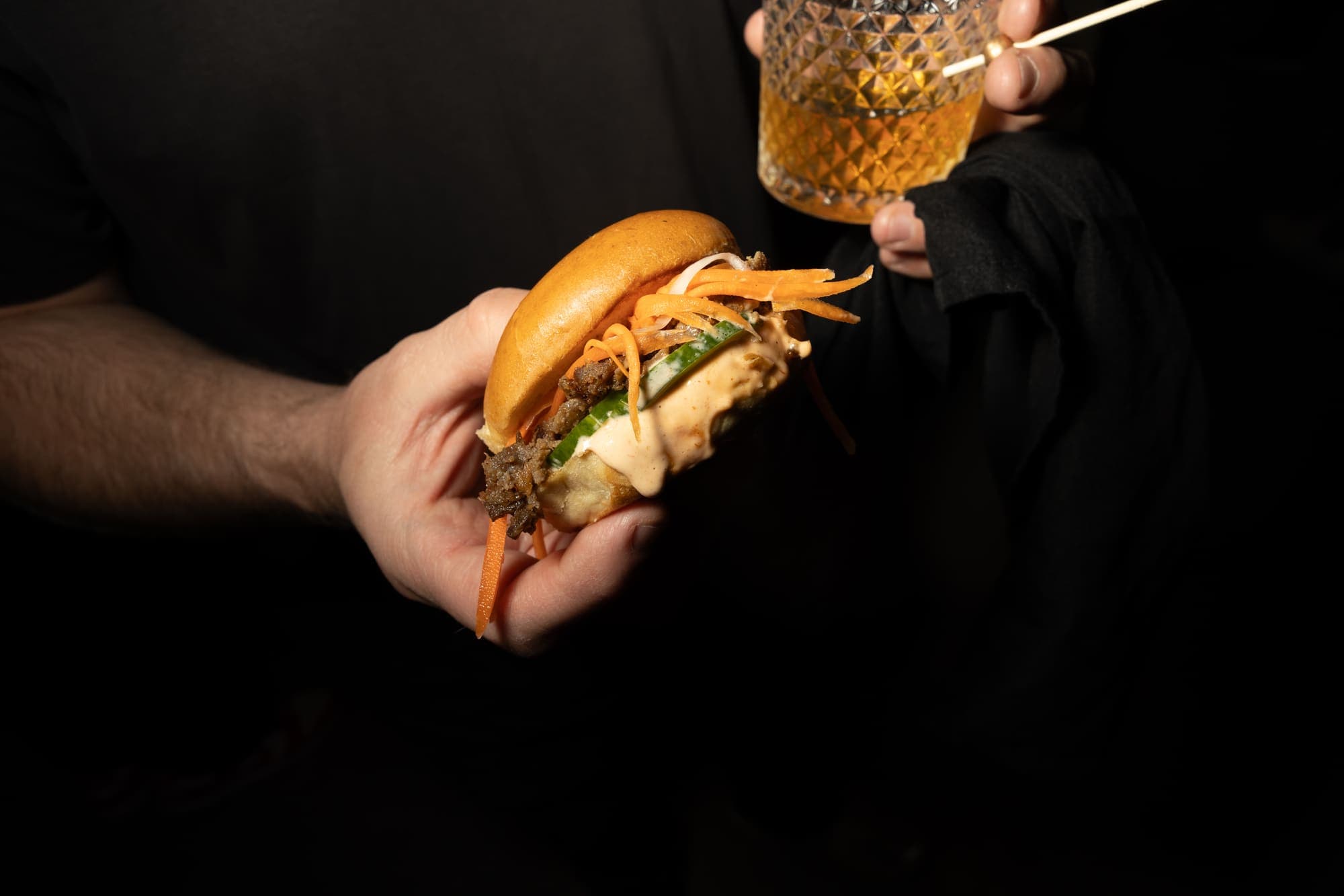 Guest holding a banh mi slider and a cocktail at a private event