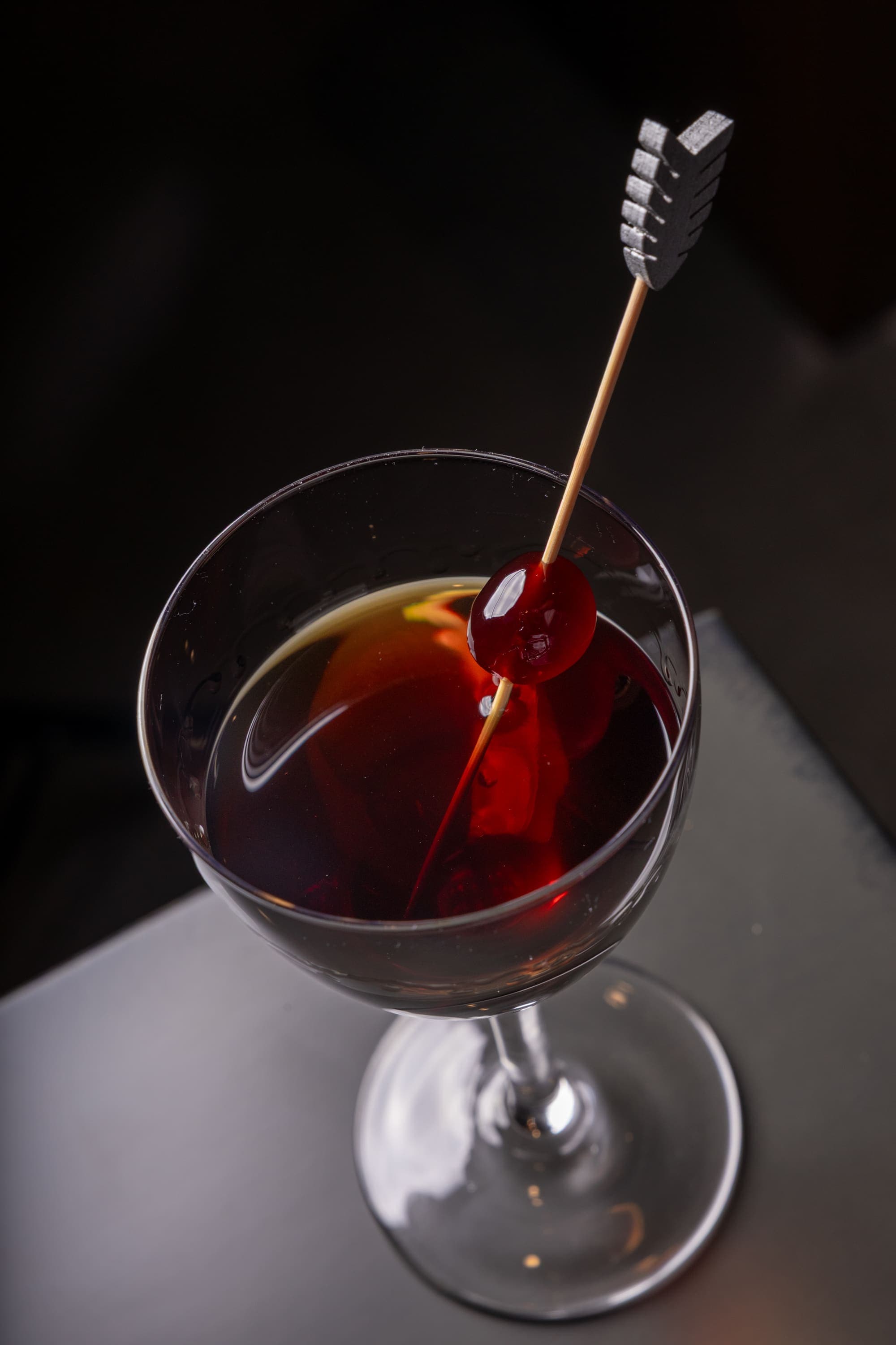 A Manhattan cocktail garnished with a cherry on an arrow pick